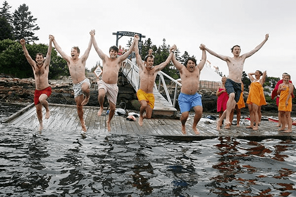 Group of young people jumping off a dock at a Maine family resort.